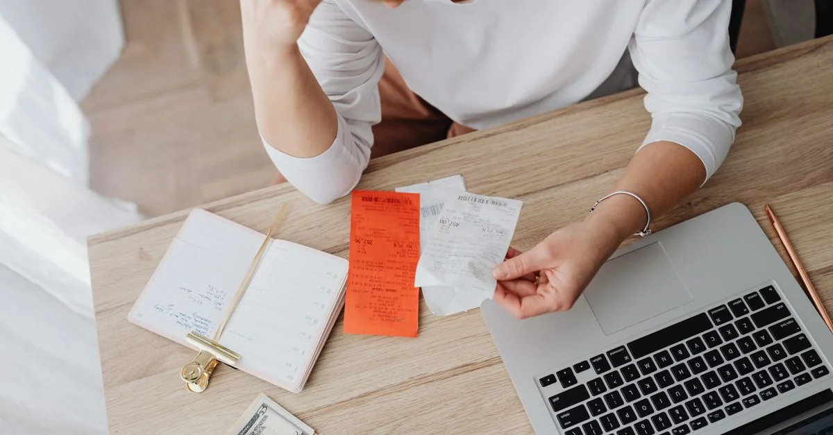Femme examinant des reçus et planifiant son budget à l'aide d'un ordinateur portable et d'un carnet à la maison pour gérer ses dépenses.