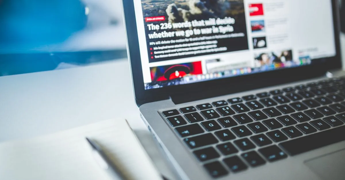 Ordinateur portable ouvert affichant un article de presse en ligne sur un bureau avec un carnet à proximité.