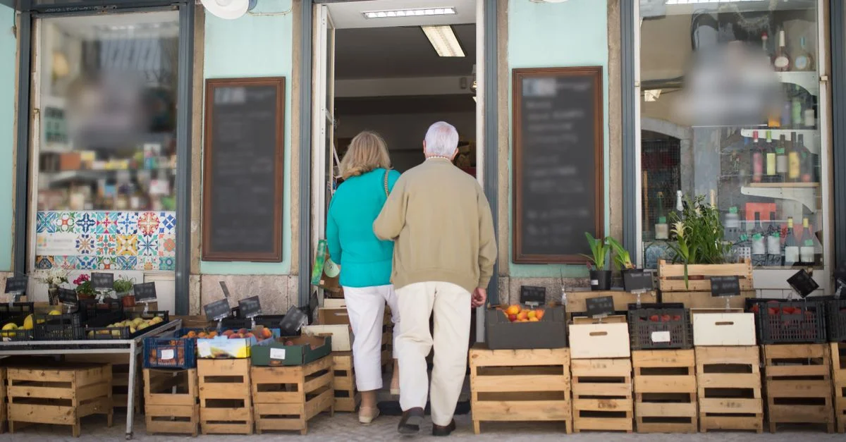 Couple âgé entrant dans une boutique portugaise locale entourée de caisses de produits frais.