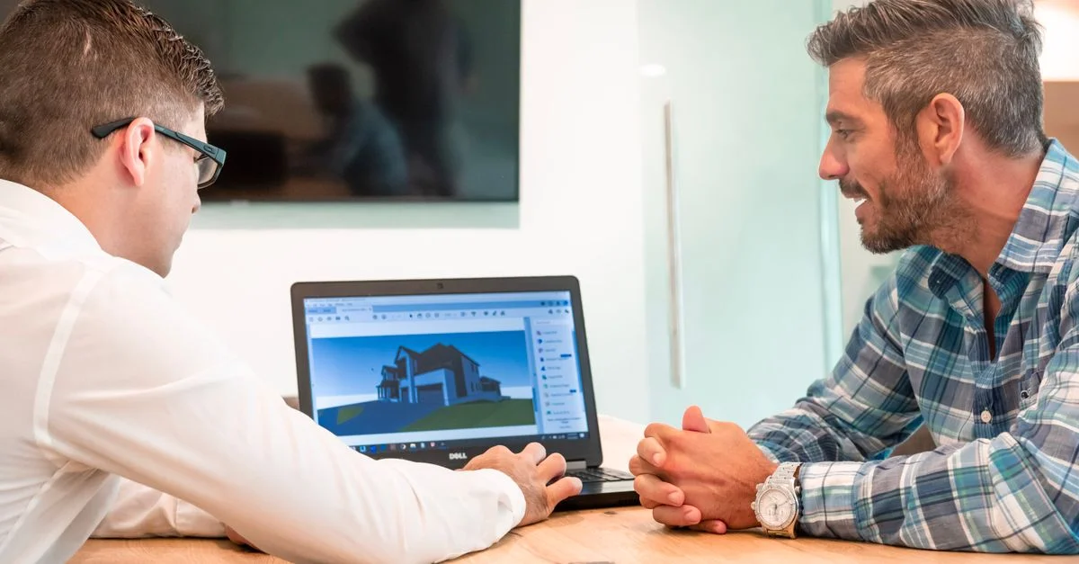 Deux professionnels discutent d'un design architectural 3D sur un ordinateur portable dans un bureau moderne.