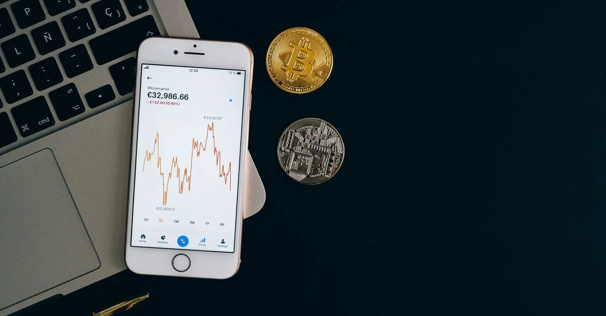 Smartphone affichant le graphique du prix du Bitcoin avec des pièces de Bitcoin et d'Ethereum sur fond noir.